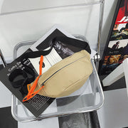 Beige crossbody sling bag with bright orange zipper pulls, displayed on a transparent chair for a modern aesthetic.