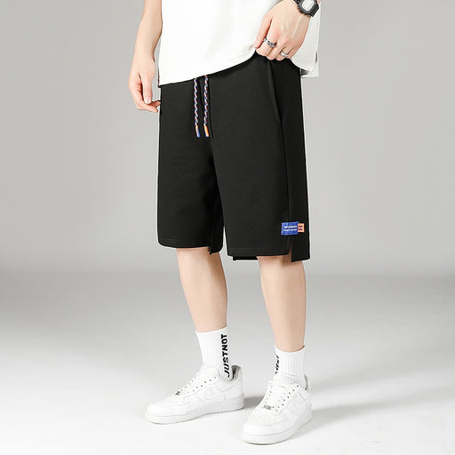 Man wearing black Korean-fit quick-dry sports shorts, styled with a white T-shirt and white sneakers, standing against a light gray background.