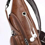 Close-up of the brown leather sling bag showing the earphone hole, smooth zippers, and detailed stitching.