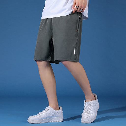 Man wearing gray Korean-fit quick-dry sports shorts, styled with a white T-shirt and white sneakers, standing against a blue studio background.
