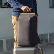 Man holding a dark gray Kingsons backpack placed on top of a suitcase, ideal for travel and daily commuting.