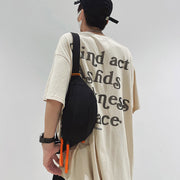 Man wearing a black crossbody sling bag with orange zipper pulls, styled over an oversized graphic T-shirt.