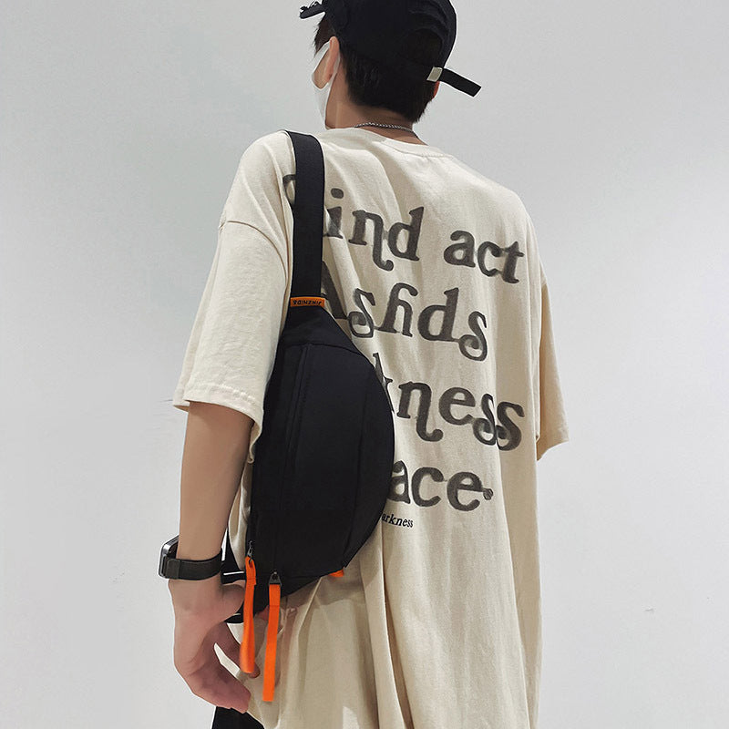 Man wearing a black crossbody sling bag with orange zipper pulls, styled over an oversized graphic T-shirt.