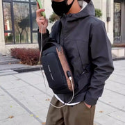 Man wearing a waterproof anti-theft USB charging crossbody bag in black and brown while walking outdoors.

