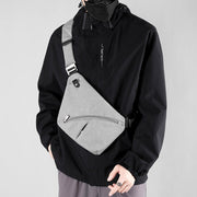 Male model wearing a gray tactical sling bag across the chest, styled with a black jacket for an urban look.

