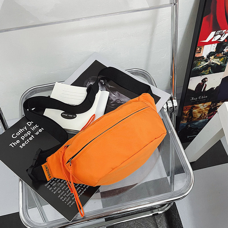 Vibrant orange crossbody sling bag with matching zipper pull, placed on a clear chair with fashion magazines.