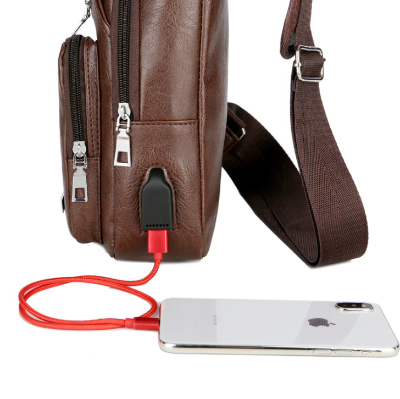 Close-up of the brown sling bag’s external USB port connected to a phone charging cable.