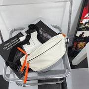 White crossbody sling bag with orange zipper pulls, displayed on a transparent chair with magazines.