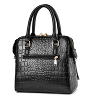 Back view of black crocodile embossed handbag featuring rear zip pocket and double top handles
