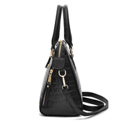 Side view of black crocodile embossed handbag with zippered pocket and adjustable shoulder strap
