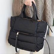 Close-up view of a black quilted winter puffer tote bag featuring soft padded construction and zippered pockets.

