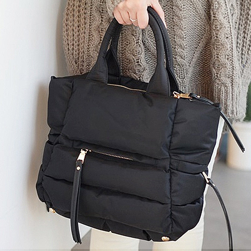 Close-up view of a black quilted winter puffer tote bag featuring soft padded construction and zippered pockets.

