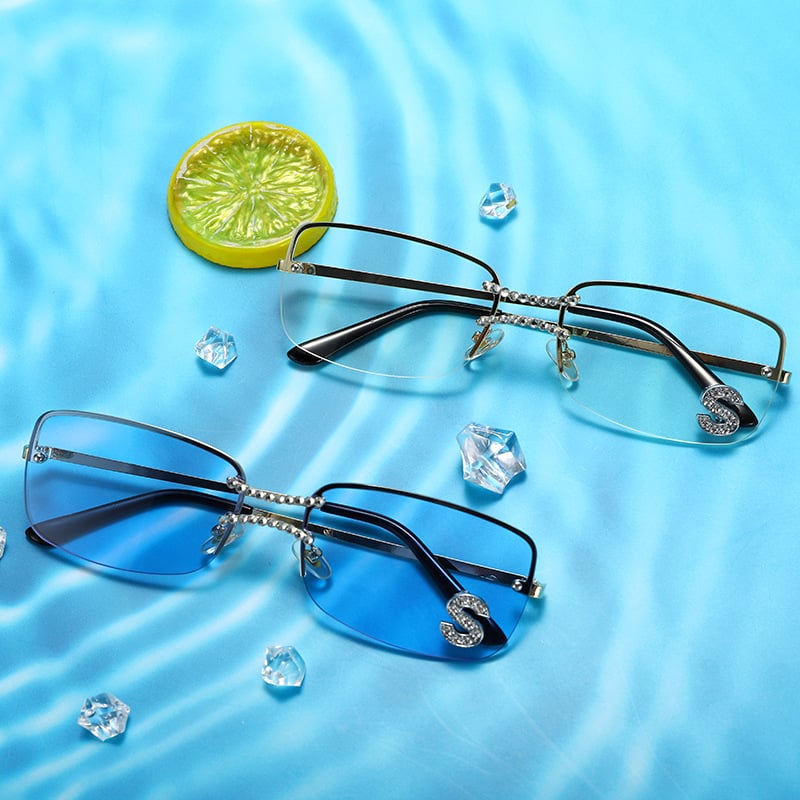 Blue and clear lens rimless sunglasses with crystal accent displayed on a luxury blue background
