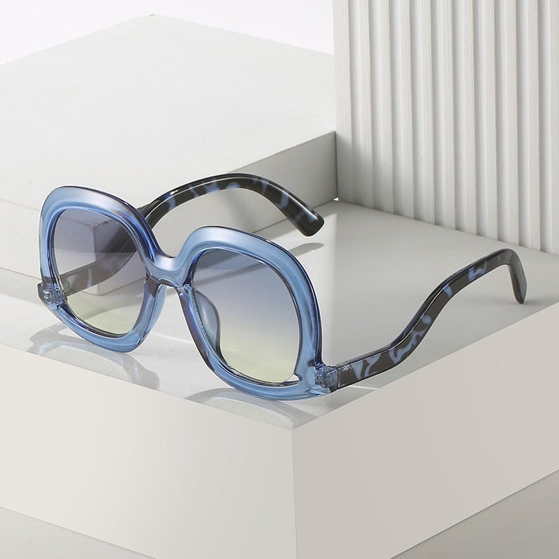Blue leopard oval sunglasses with blue yellow gradient lenses and oversized fashion frame on a clean display platform.
