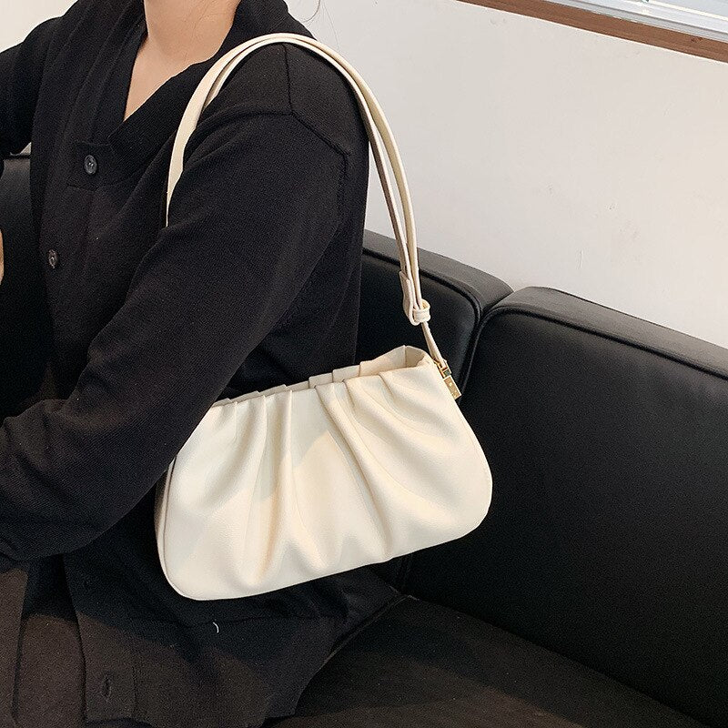 White cloud soft shoulder bag worn with a black outfit, highlighting a modern minimalist fashion accessory.

