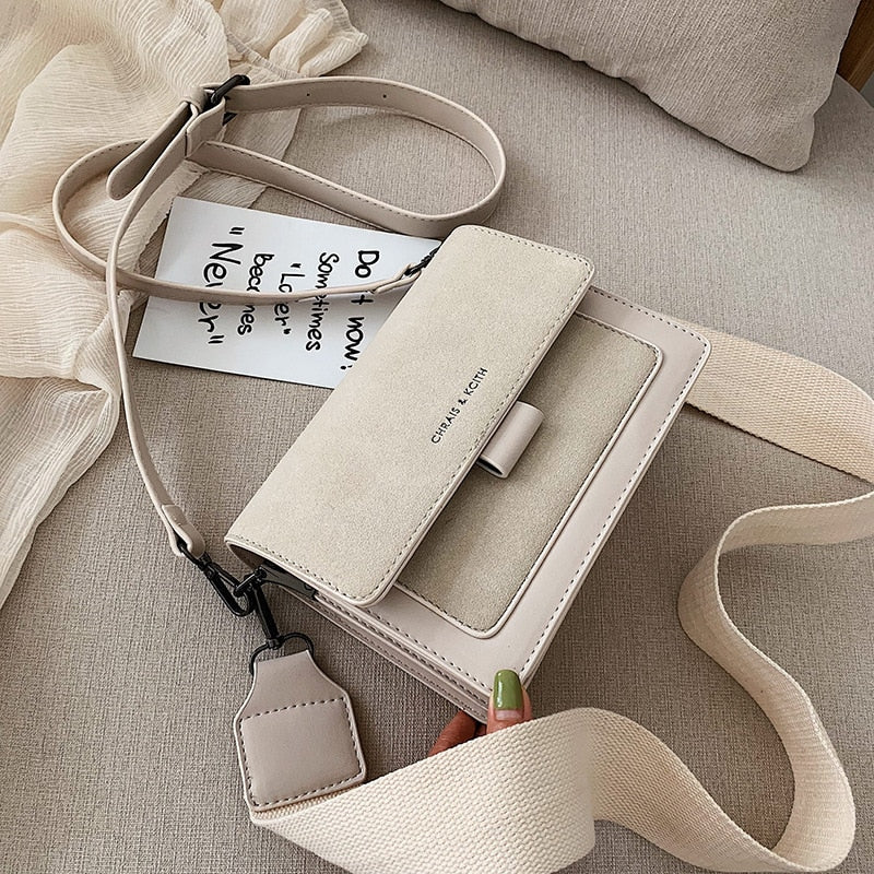 White Korean square crossbody bag with wide shoulder strap displayed on neutral fabric background
