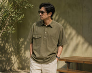 Man wearing olive green retro workwear polo shirt with dual utility pockets in a casual outdoor setting
