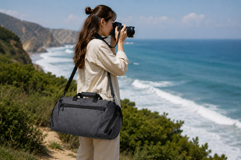 Woman using camera by the coast carrying waterproof travel and gym duffel bag
