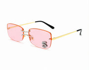 Pink lens square rimless sunglasses with gold metal frame and crystal S accent on white background
