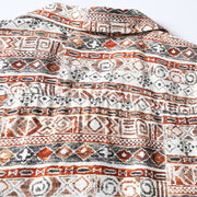 Close-up of Hawaiian print fabric featuring geometric tribal patterns in rust red, black, and cream.
