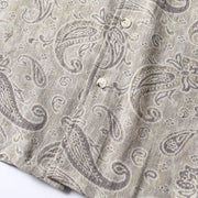 Close-up of paisley print fabric texture in beige and gray tones on men’s summer shirt.
