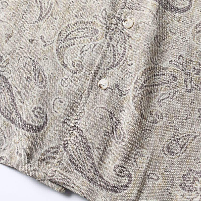 Close-up of paisley print fabric texture in beige and gray tones on men’s summer shirt.
