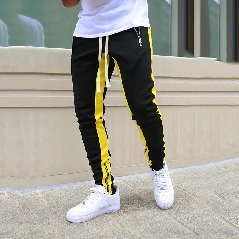 Skinny joggers for men in black with yellow stripes, styled with white sneakers for a sporty look.
