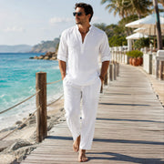Man wearing a white stand collar linen blend shirt walking along a seaside boardwalk at a luxury beach resort
