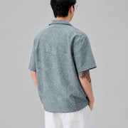 Back view of men's textured blue Cuban collar short sleeve shirt with relaxed loose fit design.
