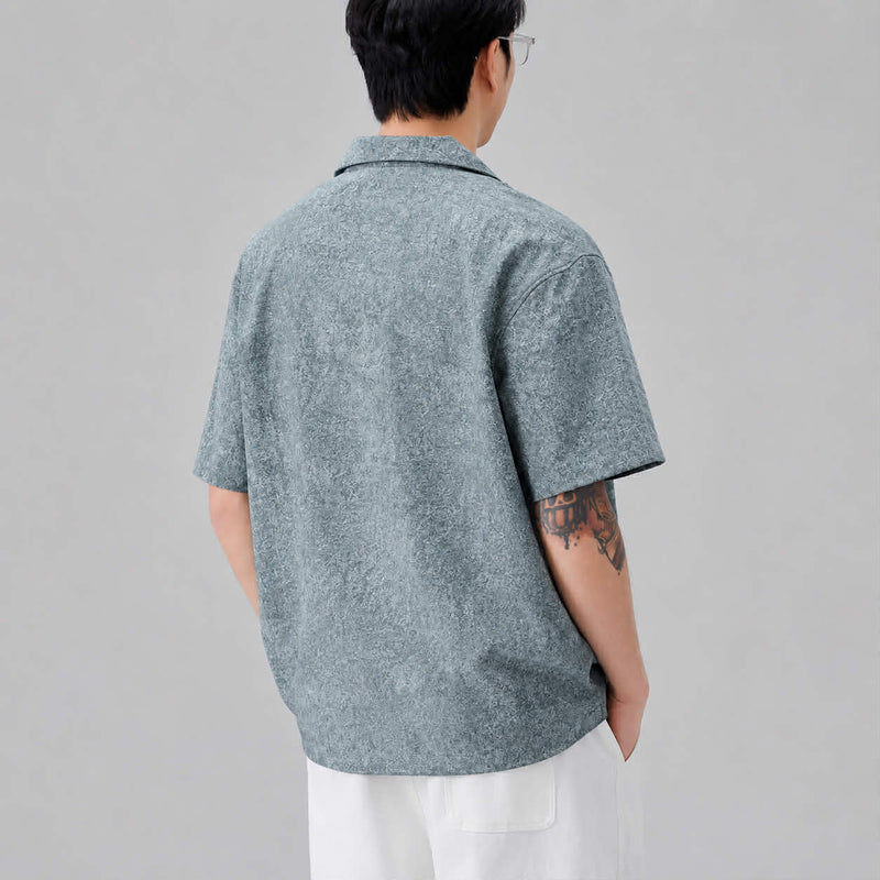 Back view of men's textured blue Cuban collar short sleeve shirt with relaxed loose fit design.
