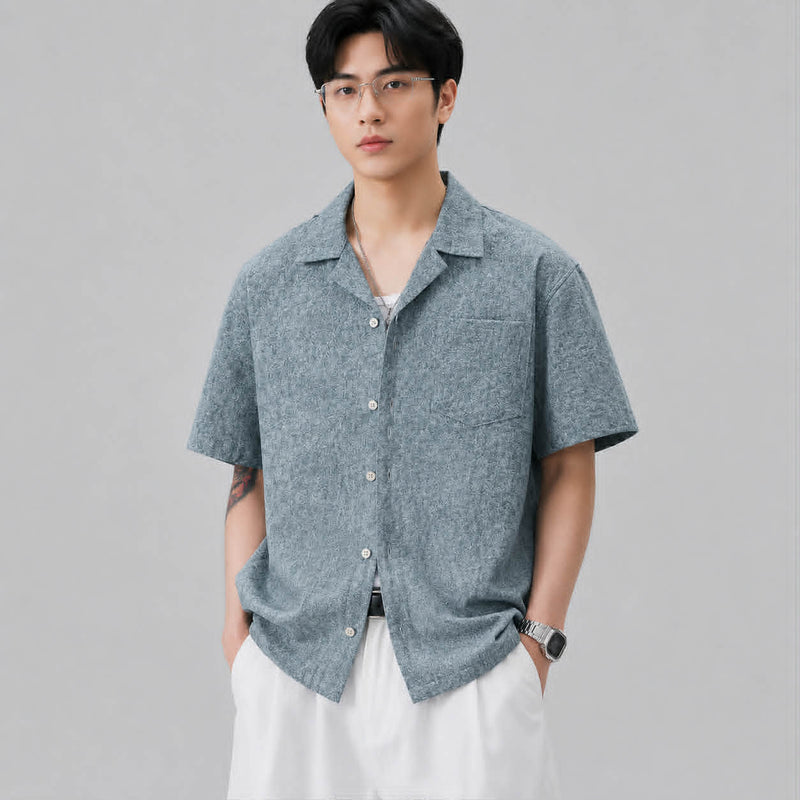 Front view of men's textured blue Cuban collar short sleeve shirt styled with white pants.
