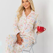 Woman relaxing with a cup of coffee while wearing a pastel floral satin pajama set.
