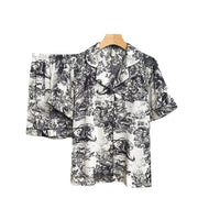 Women’s black watercolor satin pajama set with button-up short-sleeve top and matching shorts displayed flat.
