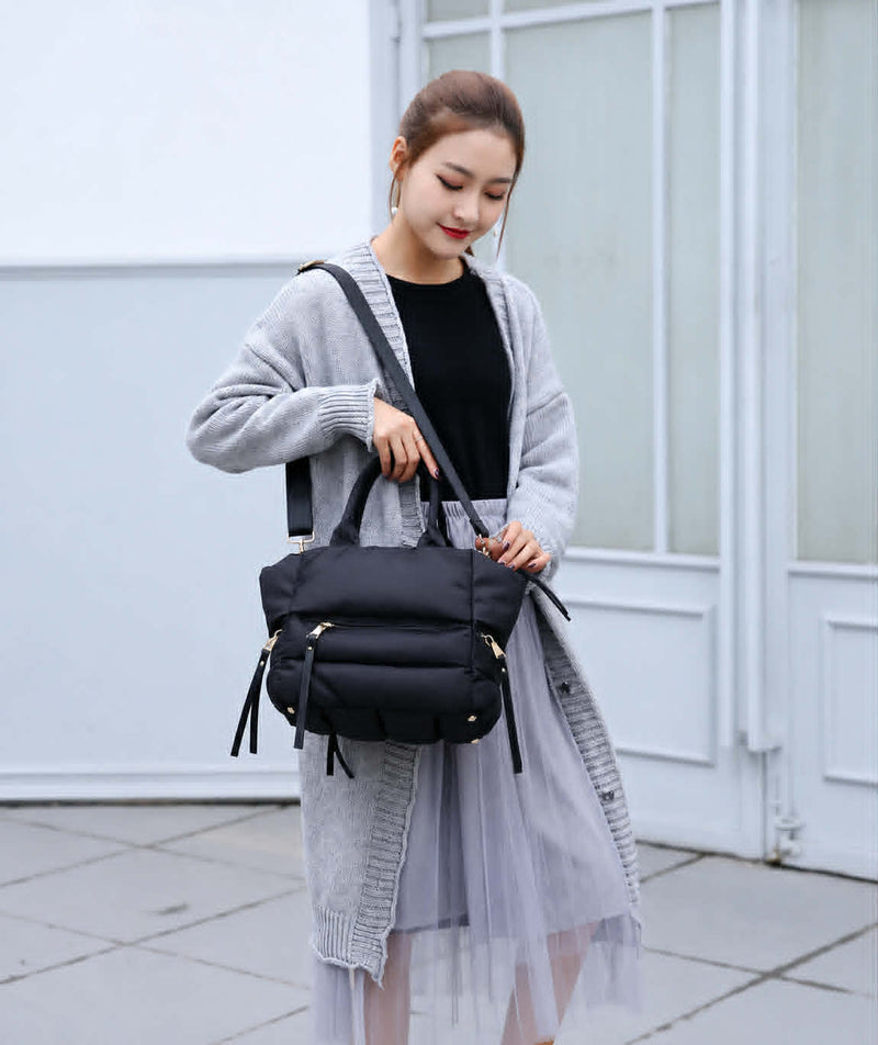 Woman carrying a black winter puffer tote bag with adjustable shoulder strap for everyday casual use.
