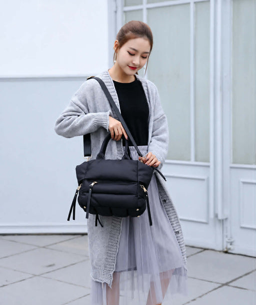 Woman carrying a black winter puffer tote bag with adjustable shoulder strap for everyday casual use.
