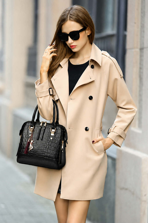 Woman wearing a black crocodile pattern handbag with gold hardware and shoulder strap
