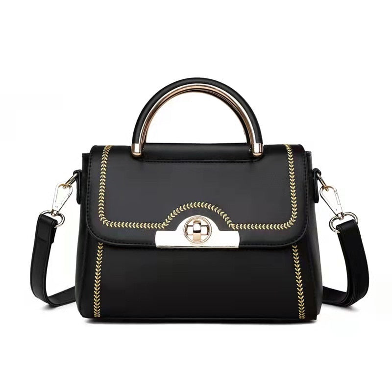 Black structured crossbody handbag with gold-tone handle and decorative stitching.

