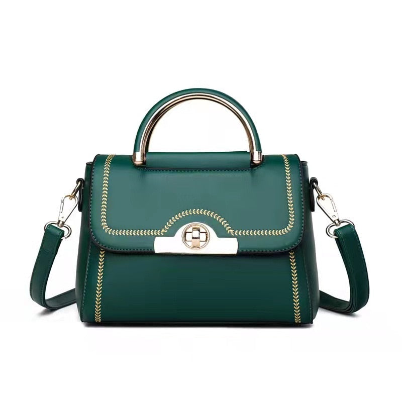 Green structured crossbody handbag with gold-tone handle and decorative stitching.
