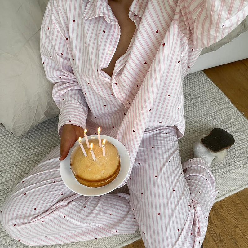 Woman wearing a soft pink long sleeve pajama set while relaxing at home with a birthday cake.
