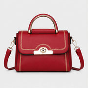 Red structured crossbody handbag with gold-tone handle and decorative stitching.
