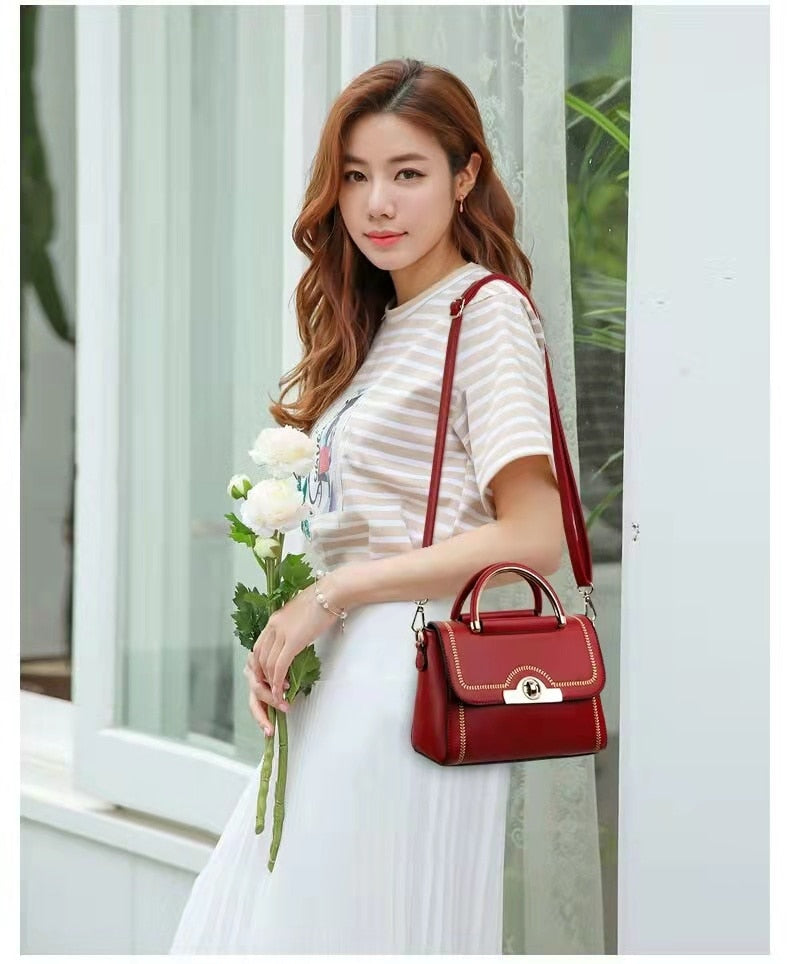 Woman carrying a red structured crossbody handbag with gold-tone handle and elegant detailing.
