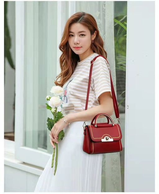 Woman carrying a red structured crossbody handbag with gold-tone handle and elegant detailing.
